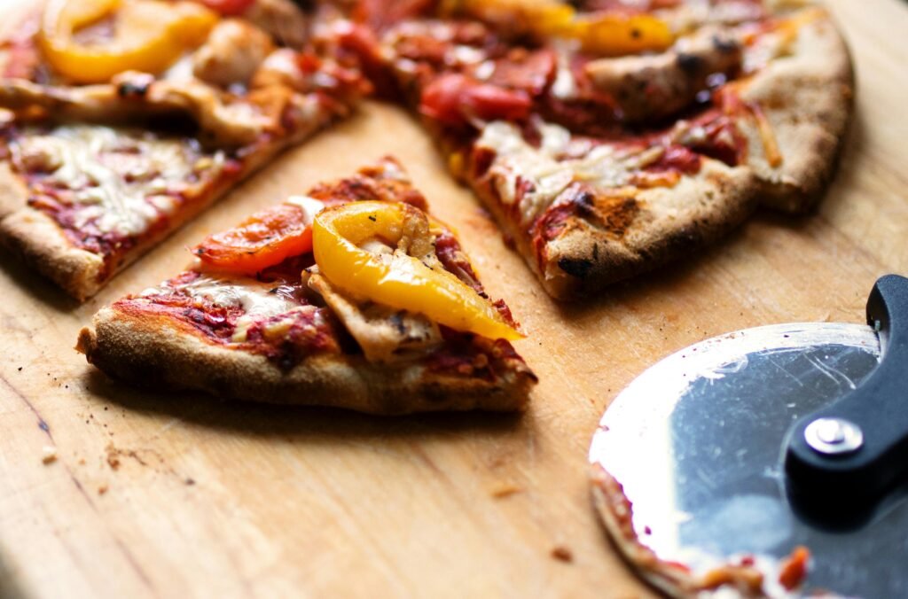 Close-up of sliced pizza with pepperoni, cheese, and bell peppers on a wooden board.